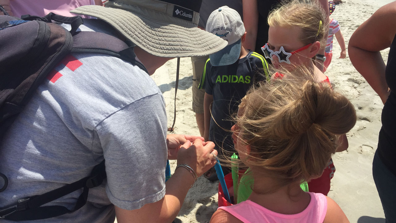 Three young children look at what is in Mendel’s hand during beach walk.